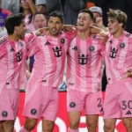 Pemain sepak bola mengenakan jersey warna pink sedang berbaris di lapangan